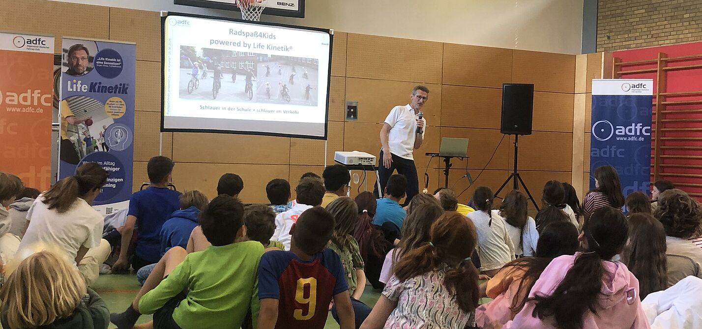 Horst-Lutz_Radspass4Kids_powered_by_Lifekinetik-Übung.JPG Life Kinetik®-Gründer Horst Lutz zeigt Bewegungsübung vor Klasse in Turnhalle vor. Er und die Kinder beugen sich nach rechts.